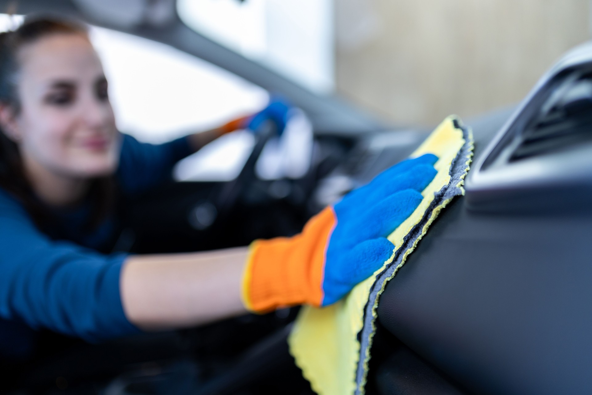 Young woman cleaning the interior of a car with a microfiber cloth while wearing colorful gloves indoors